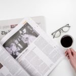 Overhead view of newspaper reading with coffee and glasses on a white table. — Baccarat: A Game That Brings Elegance, Excitem