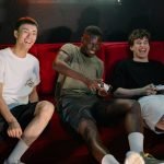 Three diverse young men sitting on a red couch, enjoying a fun video game session together. — Major Site: Access Top-Tier Cus