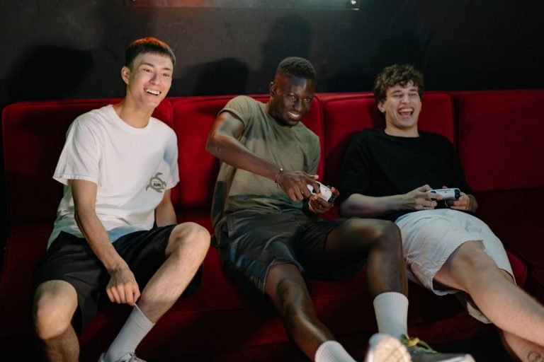 Three diverse young men sitting on a red couch, enjoying a fun video game session together. — Major Site: Access Top-Tier Cus