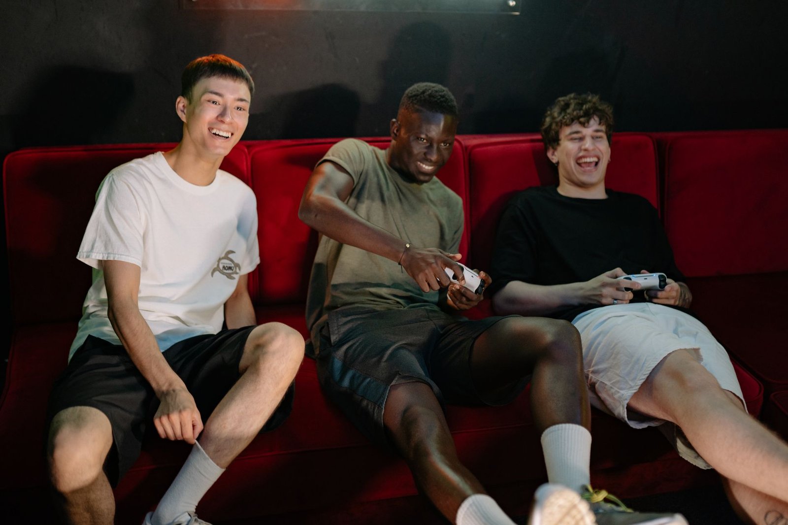 Three diverse young men sitting on a red couch, enjoying a fun video game session together. — Major Site: Access Top-Tier Cus